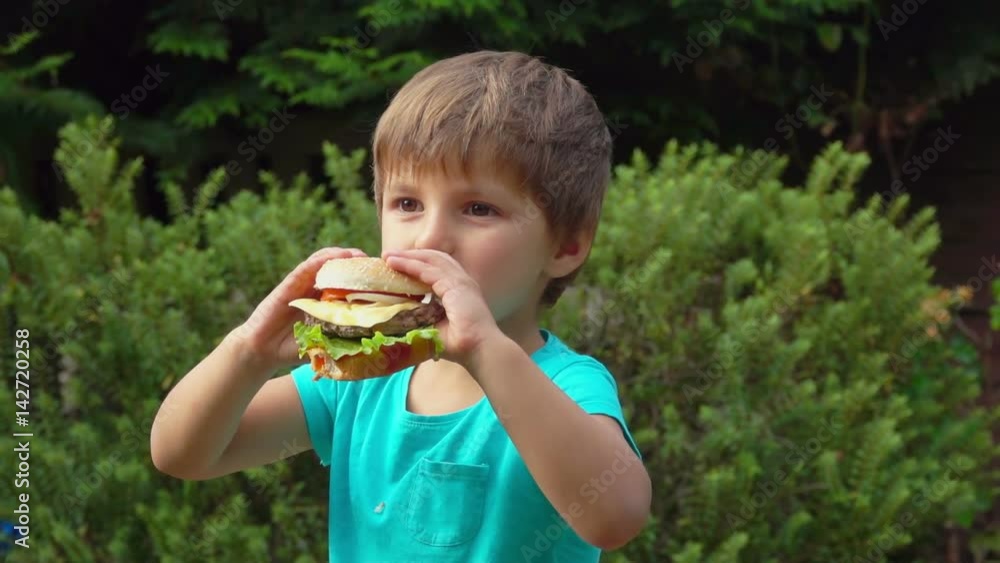 Boy eats a big juicy burger with cheese Boy eats a big juicy burger with cheese