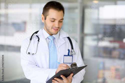 Canvas Print Male doctor filling up medical form while standing upright in hospital