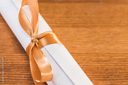 close up view of graduation university diploma with ribbon on wooden table, education concept