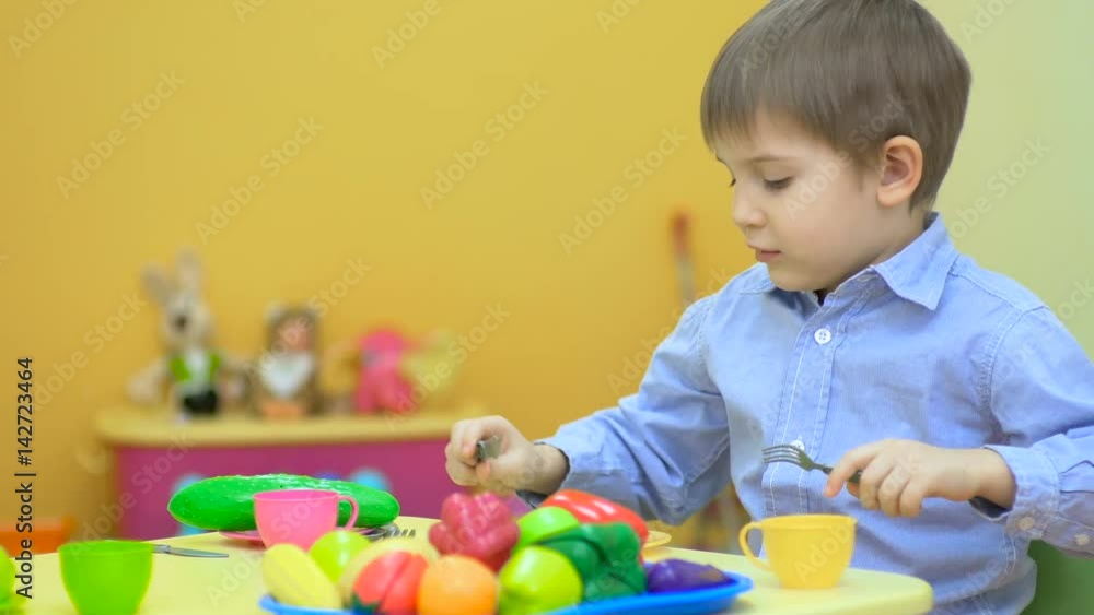 Happy little boy playing with plastic cutlery at the table Happy little boy playing with plastic cutlery at the table