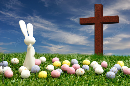 3D illustration. A white plastic bunny figurine displayed with speckled easter eggs and a wooden cross