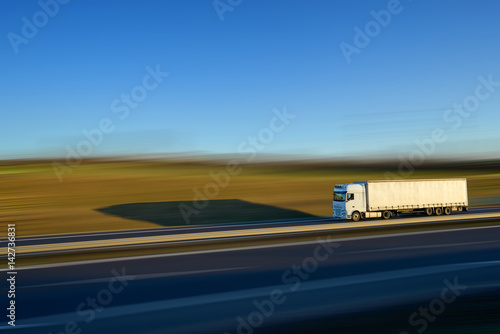 Obraz na płótnie White truck driving on the expressway and its shadow cast on abstract motion-blurred landscape on a bright sunny day w salonie