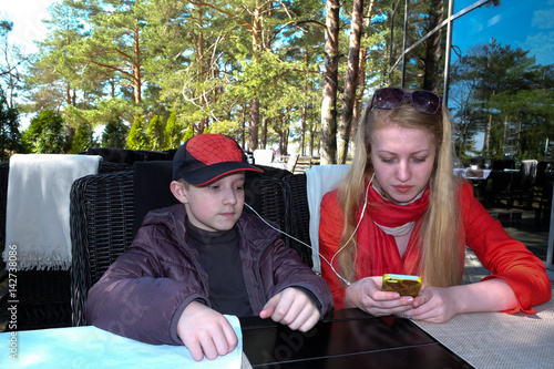 Young woman and boy listening to music outdoors at table