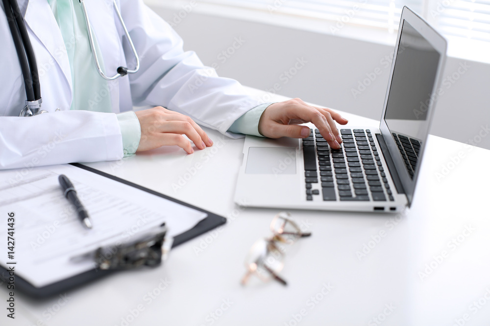 Close-up of a female doctor typing on laptop computer, sitting at the table in the hospital Close-up of a female doctor typing on laptop computer, sitting at the table in the hospital