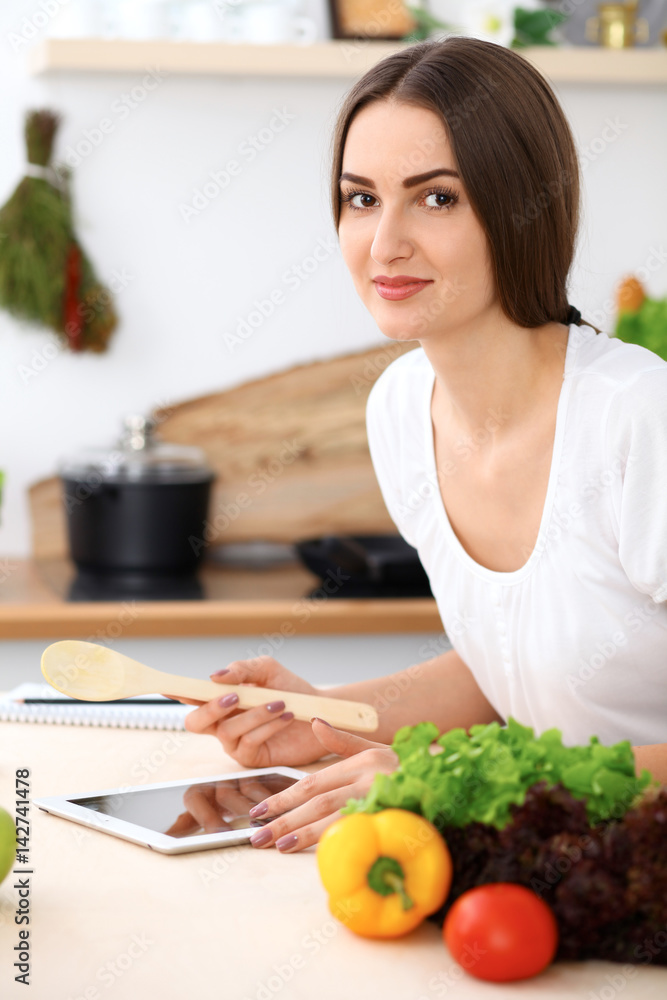 Beautiful Hispanic  woman is making online shopping by tablet computer and credit card or searching internet for a new recipe. What to cook for a dinner?