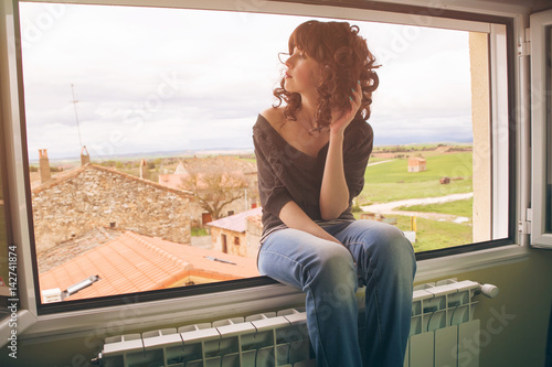 Mujer joven sentada en una ventana con unas vistas a un pueblo de fondo  photo