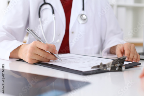 Close up of a female doctor filling up  an application form while consulting patient. Medicine and health care concept