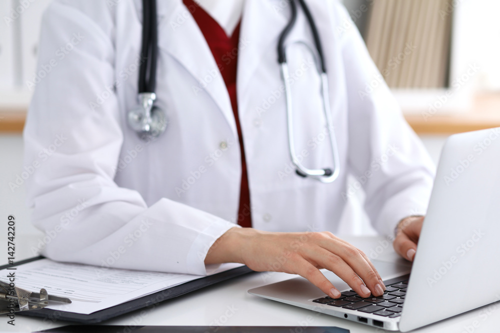 Close up of unknown female doctor typing on laptop computer while sitting at the table. Medical staff, compulsory work concept Close up of unknown female doctor typing on laptop computer while sitting at the table. Medical staff, compulsory work concept