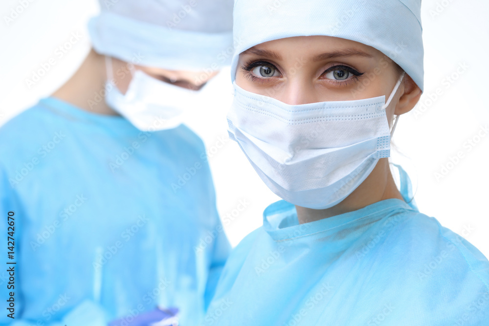 Close up of surgeon woman looking at camera while colleagues performing in background in operation room, isolated. Surgery and medicine concept Close up of surgeon woman looking at camera while colleagues performing in background in operation room, isolated. Surgery and medicine concept