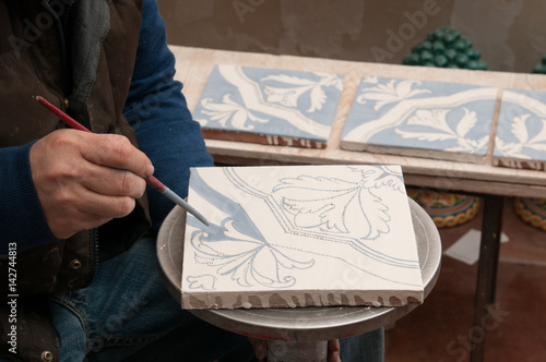 Pottery artisan in Caltagirone, Sicily, decorating just enamelled square tiles in his work table
