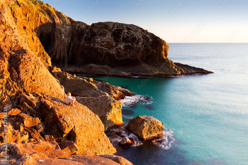 Morning light illuminates a person and a beautiful, rugged Australian ocean coastline.