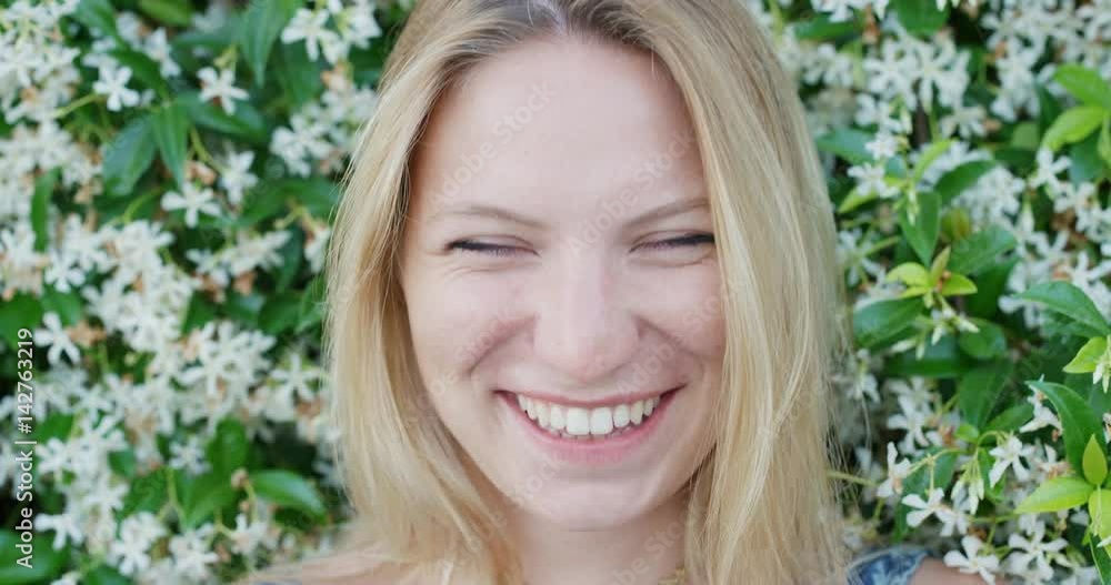 Close up portrait of beautiful young woman smiling in front of wall of flowers outdoors slow motion Close up portrait of beautiful young woman smiling in front of wall of flowers outdoors slow motion