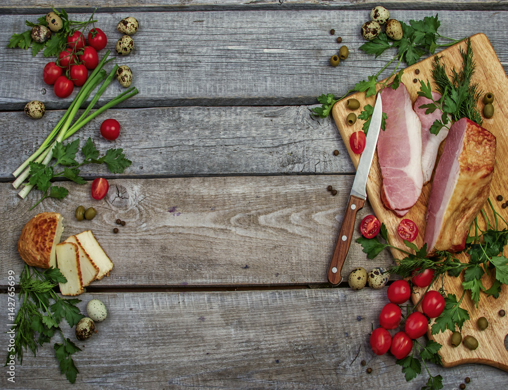 wooden background with ham, tomatoes, quail eggs, goat cheese, pepper green dill and parsley on cutting board for food blog