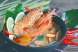 famous thai cuisine tom yum goong soup served in ceramic bowl on wooden table.