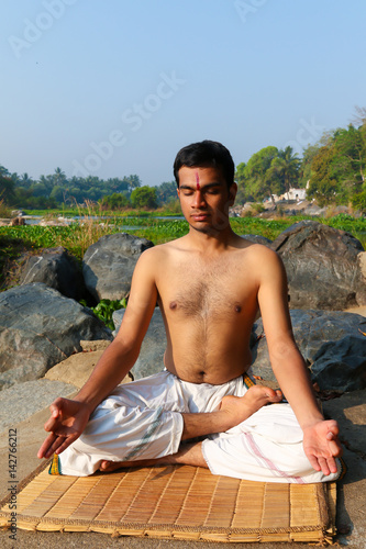 An Indian yogi meditating on a riverbank in India.