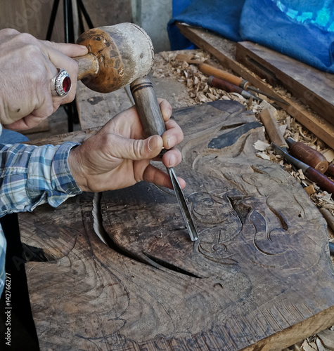 Fototapeta Wood carving. Carver with chisel and hammer