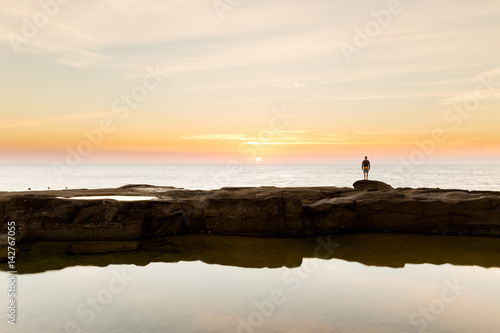 A silhouetted person watches the sunrise over the ocean on a beautiful coastline in Australia.