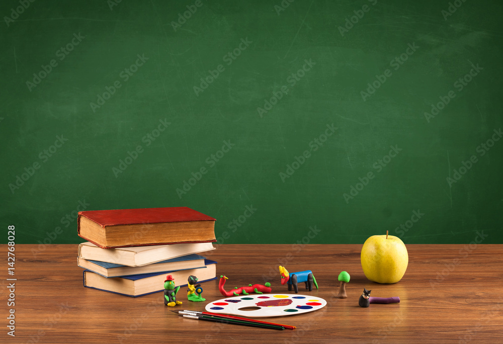 School items on desk with empty chalkboard School items on desk with empty chalkboard