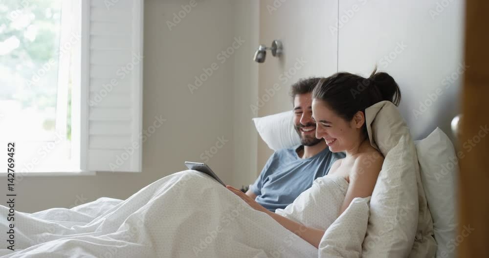 Young couple lying in bed using smartphone digital tablet technology scrolling online browsing sharing real moment morning Young couple lying in bed using smartphone digital tablet technology scrolling online browsing sharing real moment morning