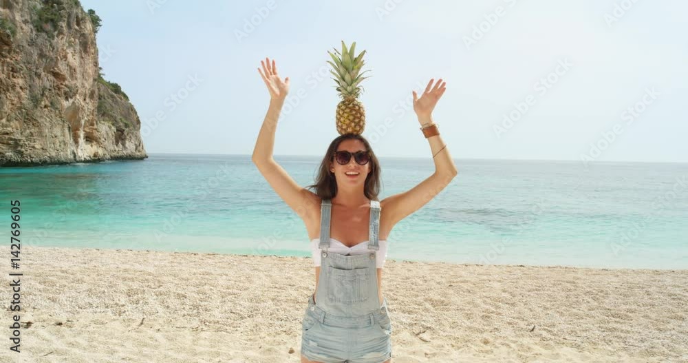Happy woman balancing pineapple on head posing for camera being silly and playful on tropical beach summer vacation holiday Happy woman balancing pineapple on head posing for camera being silly and playful on tropical beach summer vacation holiday