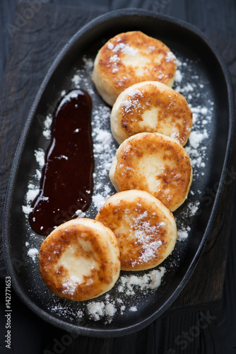 Curd pancakes or syrniki served with jam and powdered sugar in a frying pan, studio shot