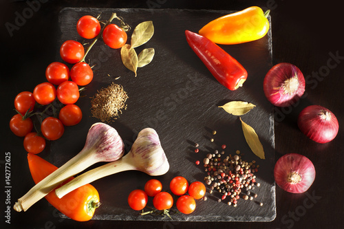 Top view of a dark board and vegetables with spices for cooking, copyspace