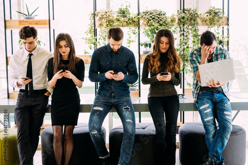 Фотография Group of friends standing on table and browsing in their divices in modern room