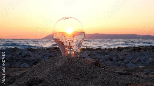 Light bulb on empty beach close to the sea at sunset, green energy concept