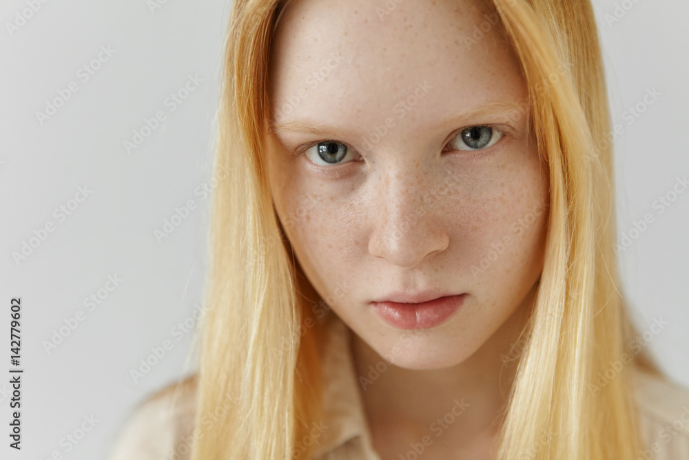 Close up highly-detailed indoor shot of extraordinary gorgeous European blonde girl with clean healthy freckled skin and blue eyes posing at studio wall with copy space for your text or advertisement Close up highly-detailed indoor shot of extraordinary gorgeous European blonde girl with clean healthy freckled skin and blue eyes posing at studio wall with copy space for your text or advertisement