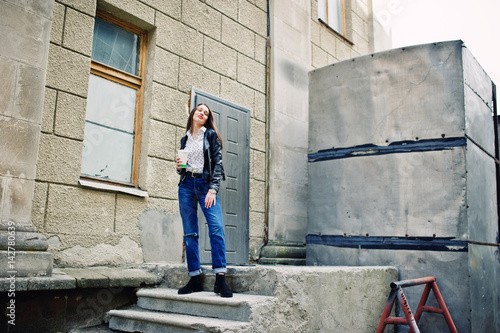 Portrait of stylish young girl wear on leather jacket and ripped jeans with cup of coffee. Street fashion model style.