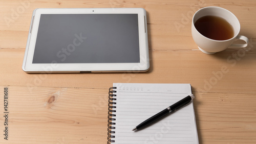 Tablet and cup of coffee with notpad,pen at workplace.