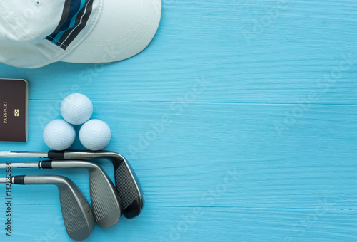 Golf clubs, golf balls, cap, passport on blue wooden table, with copy space.