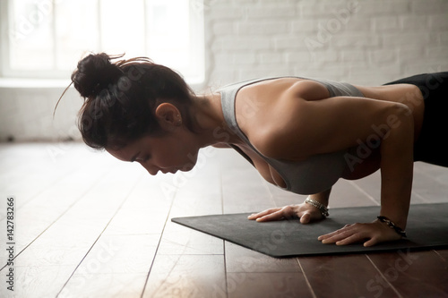 Young attractive woman practicing yoga, standing in chaturanga dandasana exercise, four limbed staff, Push ups or press ups pose, working out, white loft studio background, closeup photo