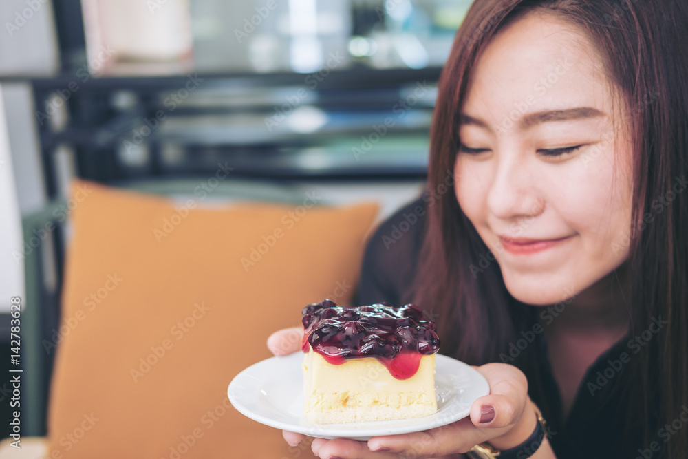 A beautiful asian woman holding blueberry cheese cake with feeling happy and good lifestyle in modern cafe A beautiful asian woman holding blueberry cheese cake with feeling happy and good lifestyle in modern cafe