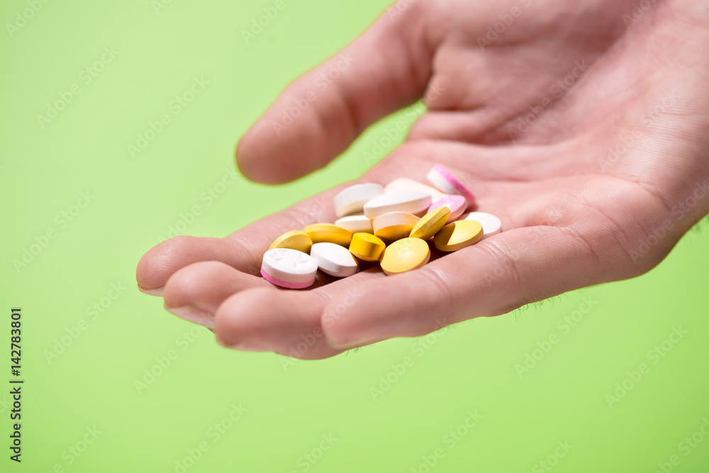 Colored pills in hand on green background.
