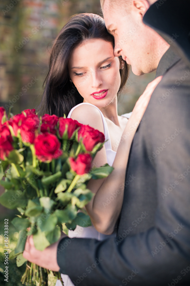 Portrait of appealing couple with roses on which woman looks at roses, man looks at woman Portrait of appealing couple with roses on which woman looks at roses, man looks at woman