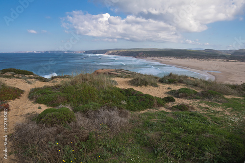 wonderful overhanging view on atlantic coastline on bordeira sandy beach in blue sky with clouds and waves, popular surf spot in algarve, portugal