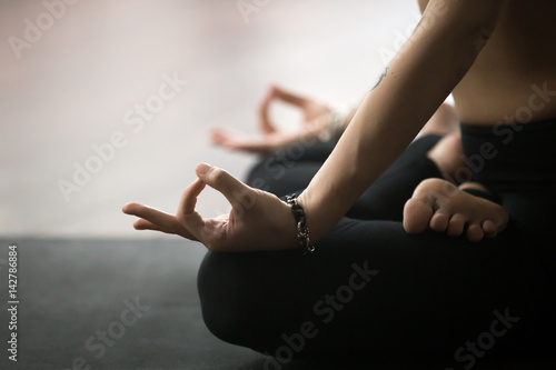 Young yogi woman practicing yoga concept, sitting in Padmasana exercise in studio or at home, Lotus pose with mudra gesture, working out on black mat, wearing sportswear pants, close up of hands