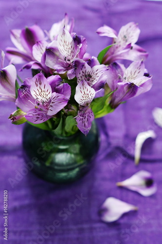 A bouquet of fresh purple flowers in a green vase on a purple background of flax 