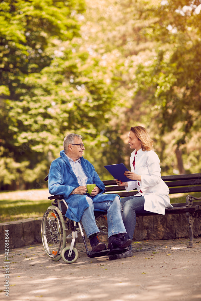 nurse talking with patient in wheelchair checking up the history of the disease outdoor. nurse talking with patient in wheelchair checking up the history of the disease outdoor.