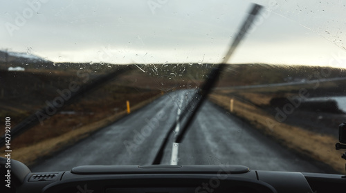 On the road in rainy day, car windshield with wipers cleaning rain drops