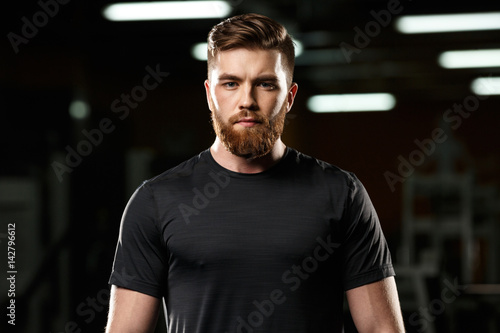 Serious handsome sports man standing and posing in gym