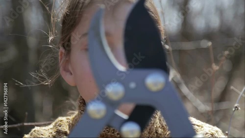 The boy cuts the trees in the garden with a pruner. The child helps to trim the trees in the park in the spring.
 photo