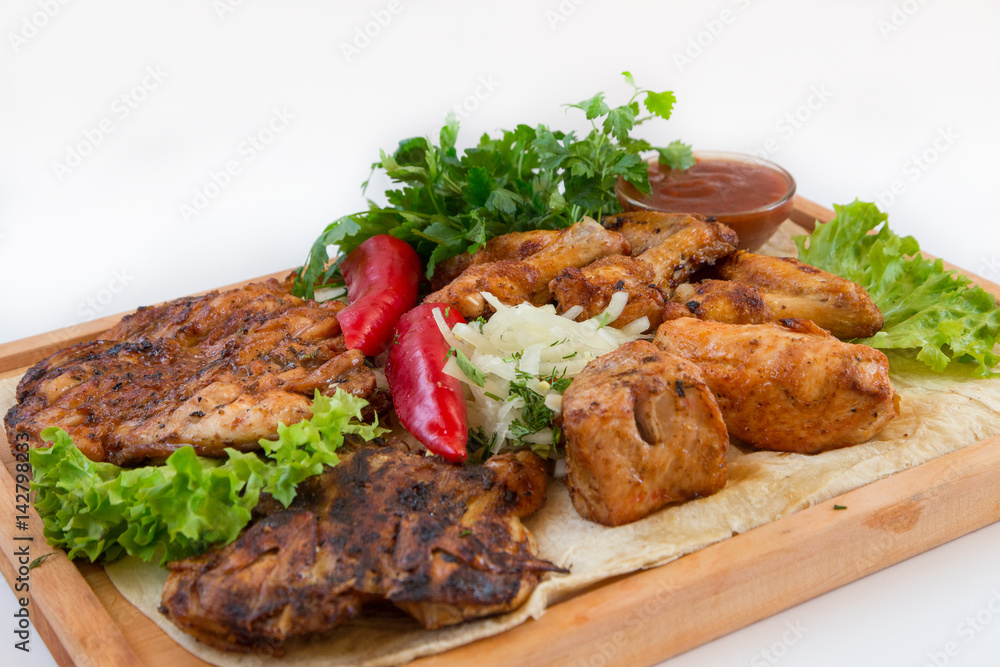 Meat dish. Pieces of roasted meat, parsley, sauce, red pepper, lettuce leaves lie on a wooden board. Isolated on white background