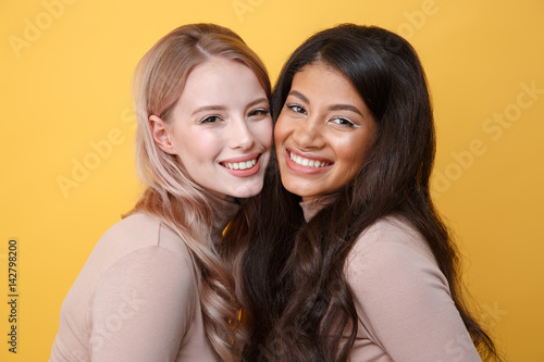 Happy young two ladies standing over yellow background