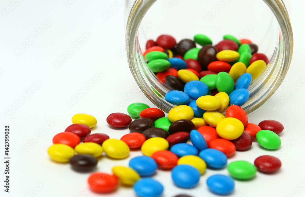 Colorful sugar-coated chocolate smarties in a glass jar on a white background Colorful sugar-coated chocolate smarties in a glass jar on a white background