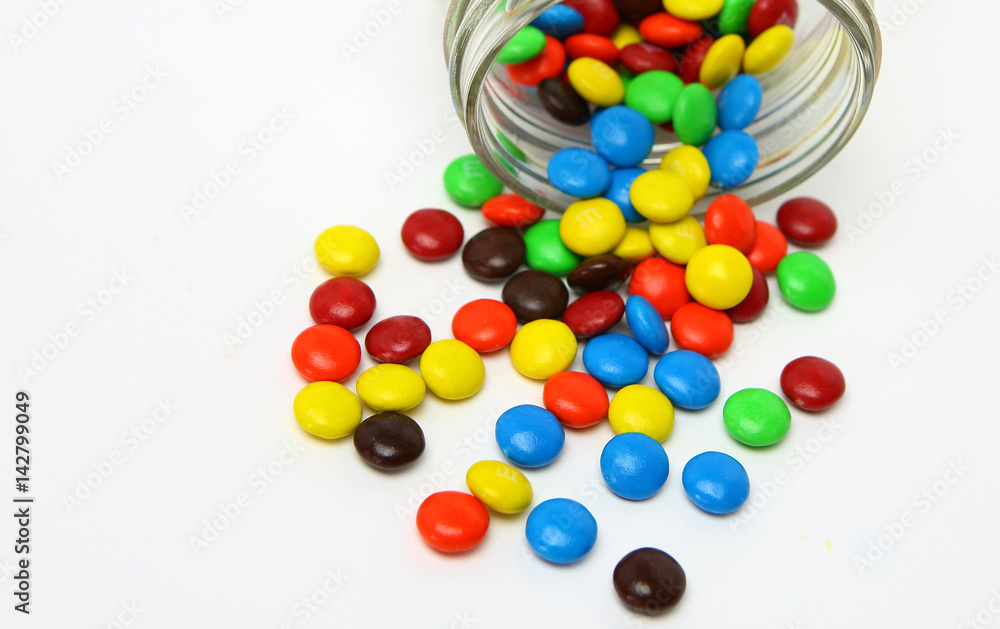 Obraz premium Colorful sugar-coated chocolate smarties in a glass jar on a white background