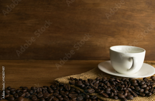 Coffee bean and cup of coffee on wooden board in front of brown