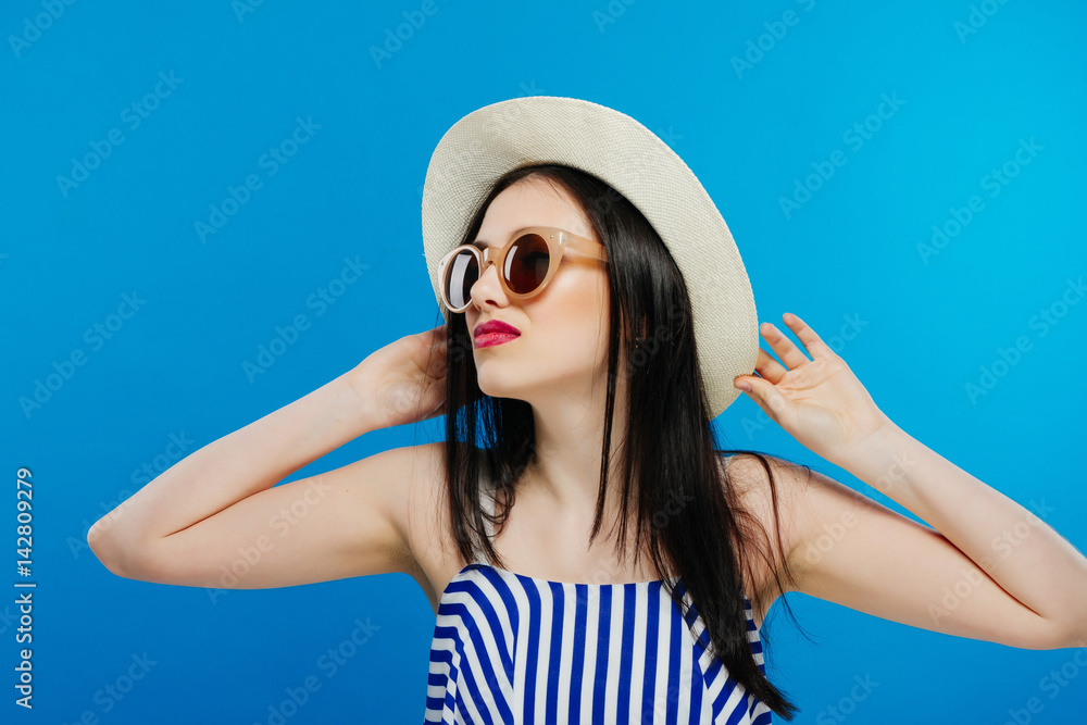 Cheerful beautiful girl in hat and sun glasses. Smiling widely, looking and pointing aside. Summer outfit. Waist up, studio, indoors Cheerful beautiful girl in hat and sun glasses. Smiling widely, looking and pointing aside. Summer outfit. Waist up, studio, indoors