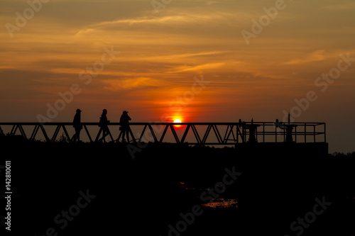 silhouette of people standing on a bridge at sunset.